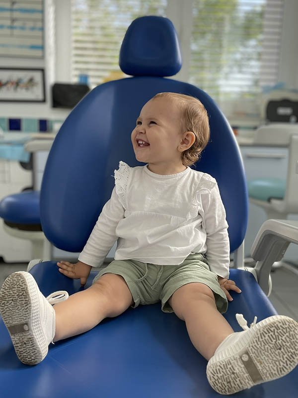 Niña pequeña sonriendo sentada en la consulta del dentista pediátrico